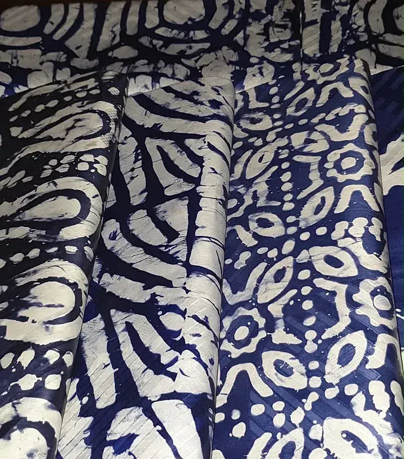Gros plan sur du bazin teinté indigo à motif dense de fleurs claires, plié en pièce.