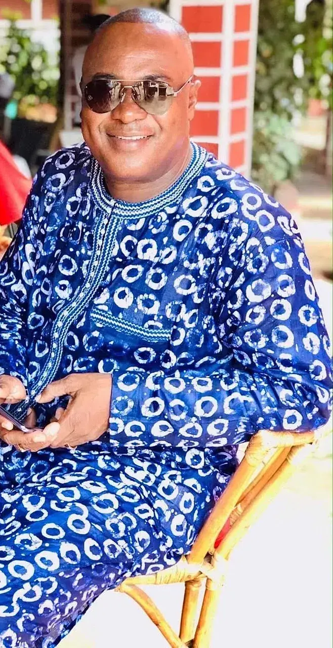 Homme assis en boubou de bazin teinté indigo, motif de cercles clairs, en lumière naturelle.