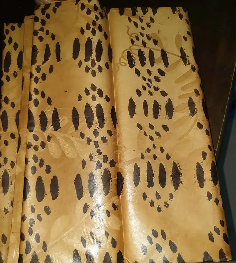 Bazin teinté jaune d’or, semé de graines sombres.