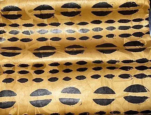 Bazin teinté ocre, motif d’ovales noirs alignés en rangées serrées.