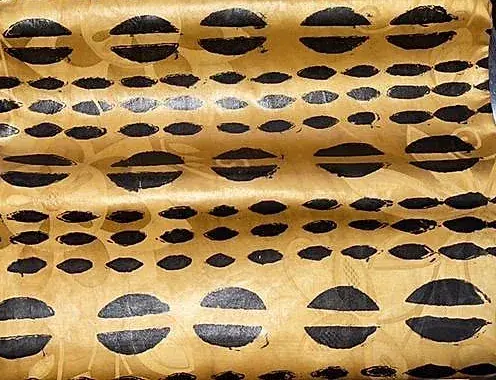 Bazin teinté ocre, motif d’ovales noirs alignés en rangées serrées.