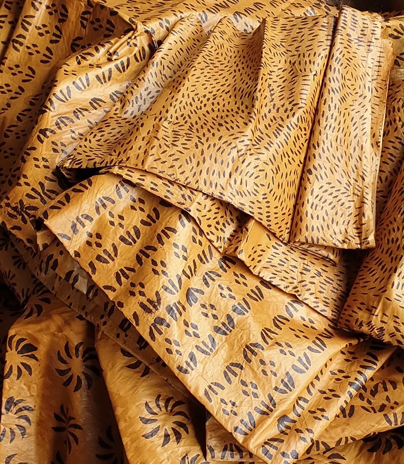 Bazin teinté jaune d’or, drapé en plis profonds, motif de graines sombres.